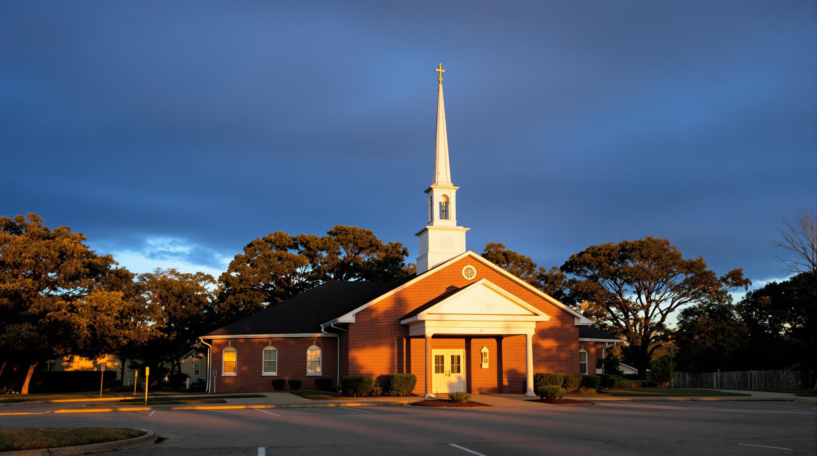 Red-brick suburban Baptist church with a white spire among live oaks in southwest Fort Worth, Texas